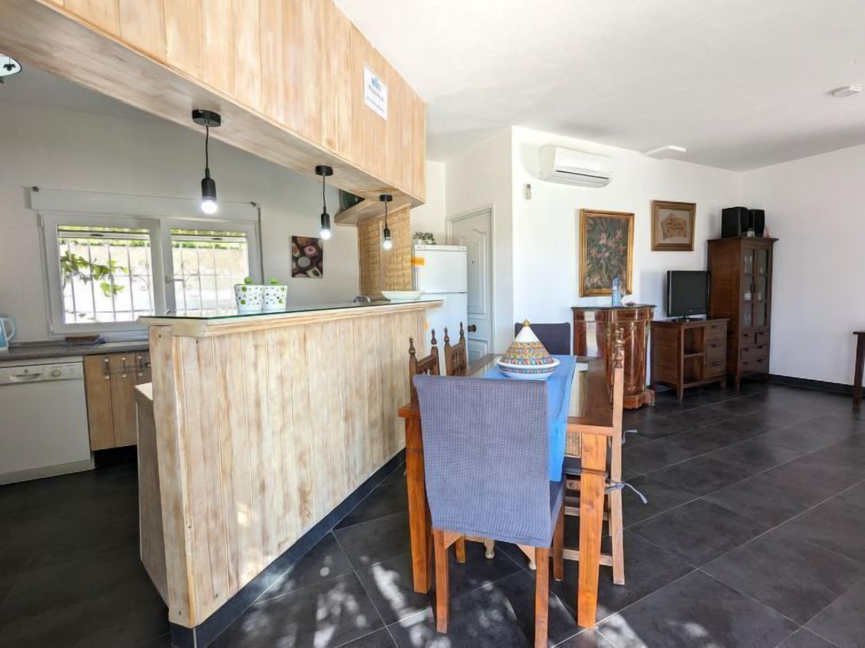 A modern kitchen with wooden cabinetry, a central island, and a dining area with a table and chairs.