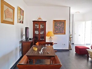 Un comedor con una mesa de madera y bancos, un armario con puertas de cristal, un televisor y un cuadro en la pared.