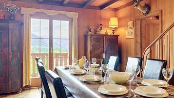A dining area with a table set for four, wooden walls, a view of the outdoors, and a chandelier.