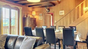 Un espace repas doté d’un plafond en bois, d’un canapé, d’une table à manger, de chaises et d’un lustre.