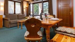 Una habitación acogedora con una mesa de comedor de madera dispuesta para dos personas, un sofá y una silla de madera con respaldo abierto.