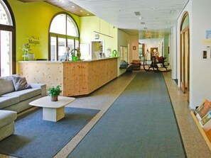 A reception area with a wooden reception desk, a sofa, a small table with a plant, and a large window.