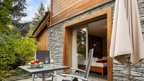 A wooden cabin with a stone exterior, a dining area with a table and chairs, and a view of the surrounding forest. - Rütschi by Interhome (Zermatt)