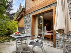 Una cabaña de madera con revestimiento de piedra, un comedor con mesa y sillas, y vistas del bosque circundante.