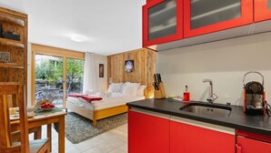 A modern bedroom with a large bed, a wooden wardrobe, and a red kitchen area with a sink and utensils. - Rütschi by Interhome (Zermatt)