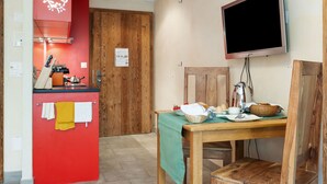 A compact kitchen with a red accent wall, a wooden door, a dining table with a green tablecloth, and a mounted television. - Rütschi by Interhome (Zermatt)