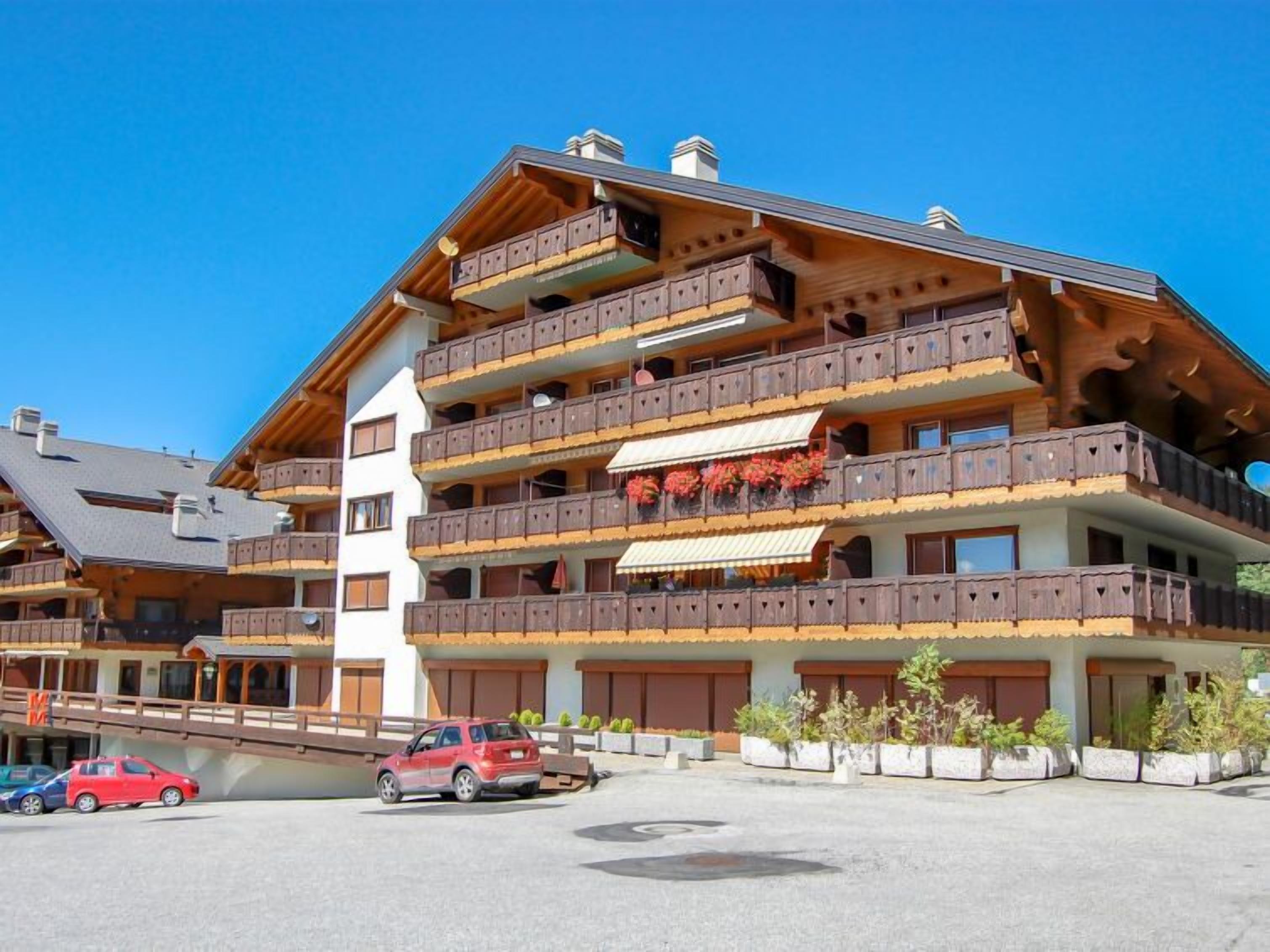 Een hotel met meerdere verdiepingen, houten balkons en een skilift in de achtergrond.