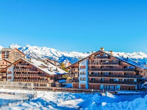 Ein Gebirgsort mit Holzbauten, schneebedeckten Bergen und blauem Himmel.