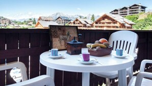 Un tavolo rotondo con un dipinto di zebre, una ciotola di frutta e due tazze su un balcone affacciato su un villaggio montano con edifici in legno.