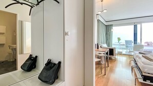 Una camera d'albergo con un letto, una scrivania e una sedia. Si vede uno specchio e un appendiabiti con una borsa.