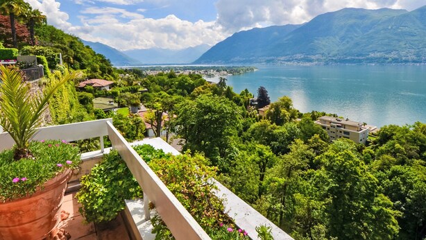 Un balcone con piante in vaso e vista su un lago e montagne.