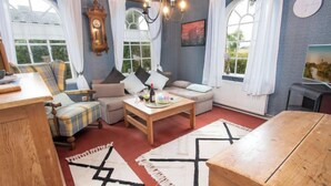 A cozy living room with a sofa, a wooden coffee table, and a dining table. There are large windows with curtains, a clock, and a painting on the wall. - Itzendorfer Rott by Interhome (Norddeich)