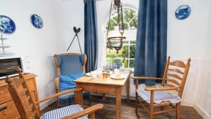 A dining area with a wooden table and chairs, a hanging light fixture, and a view through a window with curtains. - Itzendorfer Rott by Interhome (Norddeich)