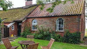 A brick house with a tiled roof, a small porch, and a grassy yard with wooden chairs and a table. - Itzendorfer Rott by Interhome (Norddeich)