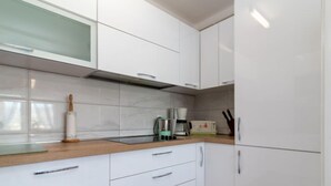 Une cuisine moderne avec des meubles blancs, un plan de travail en bois, une machine à café et un rouleau à pâtisserie.