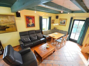 Una sala de estar con un sofá de cuero negro, una mesa de centro de madera y una mesa de comedor con sillas. Hay cuadros en las paredes y una ventana con cortinas.