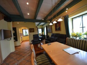 Una sala de estar acogedora con una mesa de comedor de madera, un sofá de cuero negro y un televisor montado en la pared.