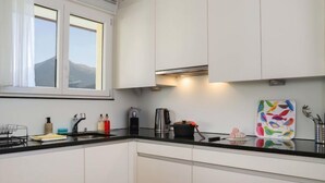 A modern kitchen with white cabinets, a black countertop, and a window with a view of a mountain. - Attika Wohnung Allod Park Haus C 807 by Interhome (Davos)