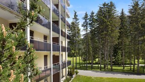 A multi-story building with balconies, surrounded by a well-maintained lawn and tall trees. - Attika Wohnung Allod Park Haus C 807 by Interhome (Davos)
