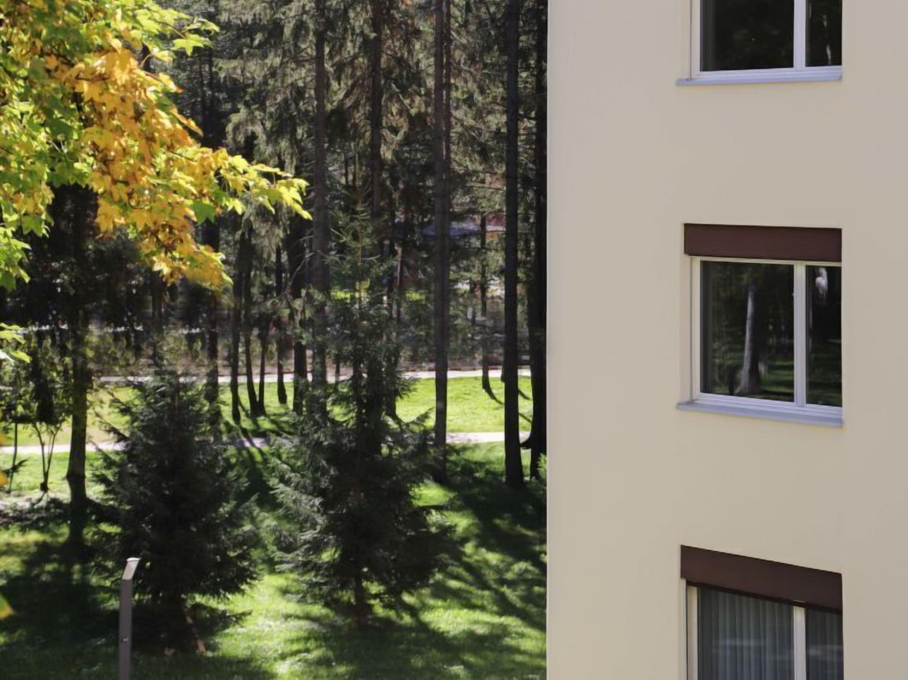 A multi-story building with a flat roof, surrounded by a well-maintained lawn and tall trees.