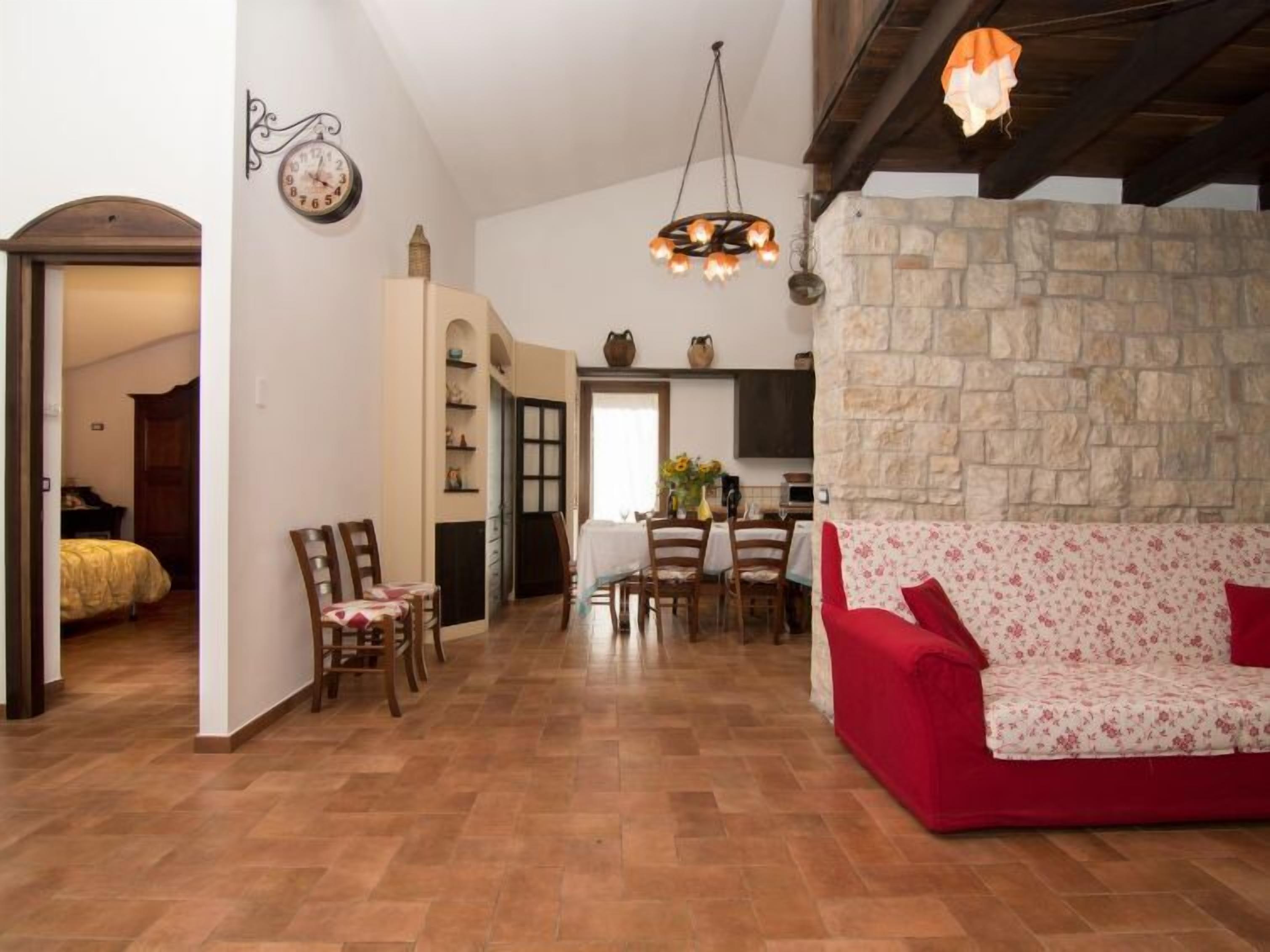 A spacious living area with a stone wall, a red sofa, and a dining table with chairs.