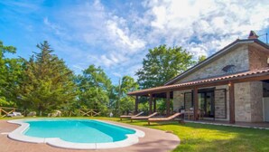 Una casa con piscina, patio cubierto y fachada de piedra.