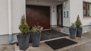 Entrada d'un edifici amb una porta de fusta, una petita zona d'seients a l'exterior i plantes en testos.