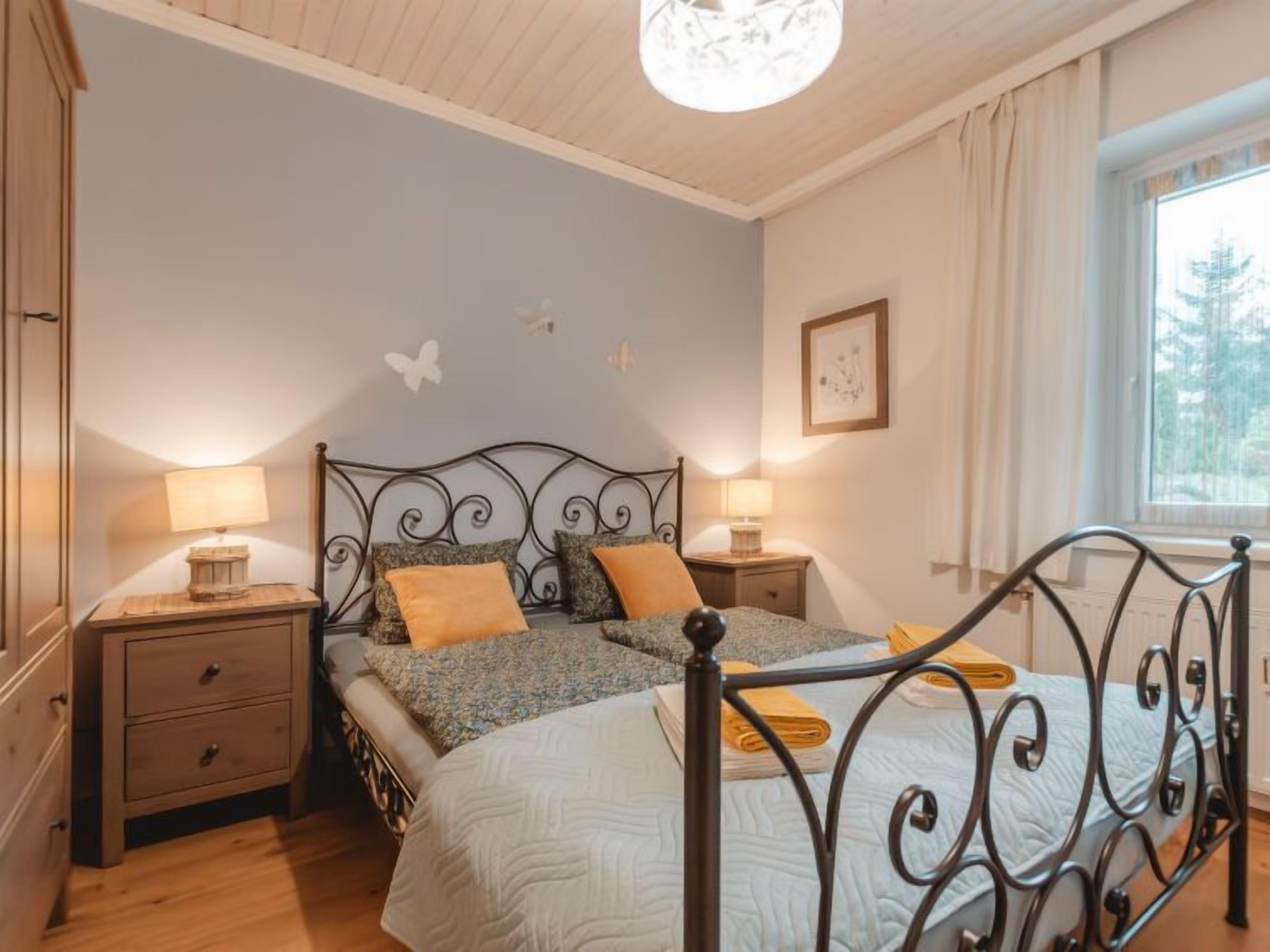 Ein Schlafzimmer mit einem Bett, zwei Nachttischen, einem Fenster und einer Deckenleuchte.
