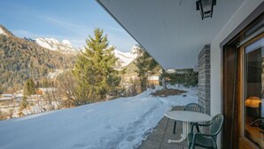 Une terrasse avec une table et des chaises donnant sur un paysage enneigé, avec des montagnes en arrière-plan.