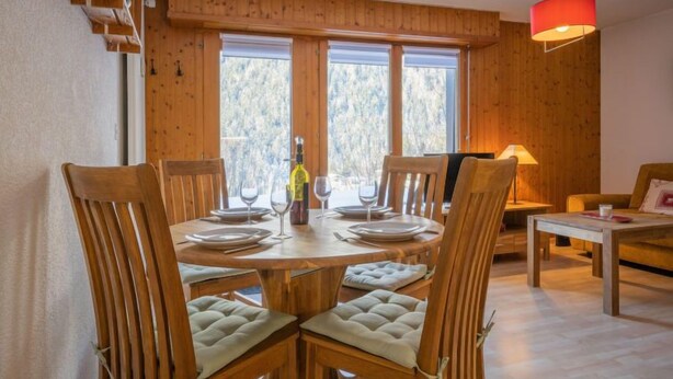 Un coin repas avec une table en bois dressée pour quatre personnes, entourée de chaises rembourrées.