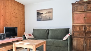 Un salon comprenant un meuble TV en bois, un canapé vert, une table en bois et un buffet doté de plusieurs tiroirs.