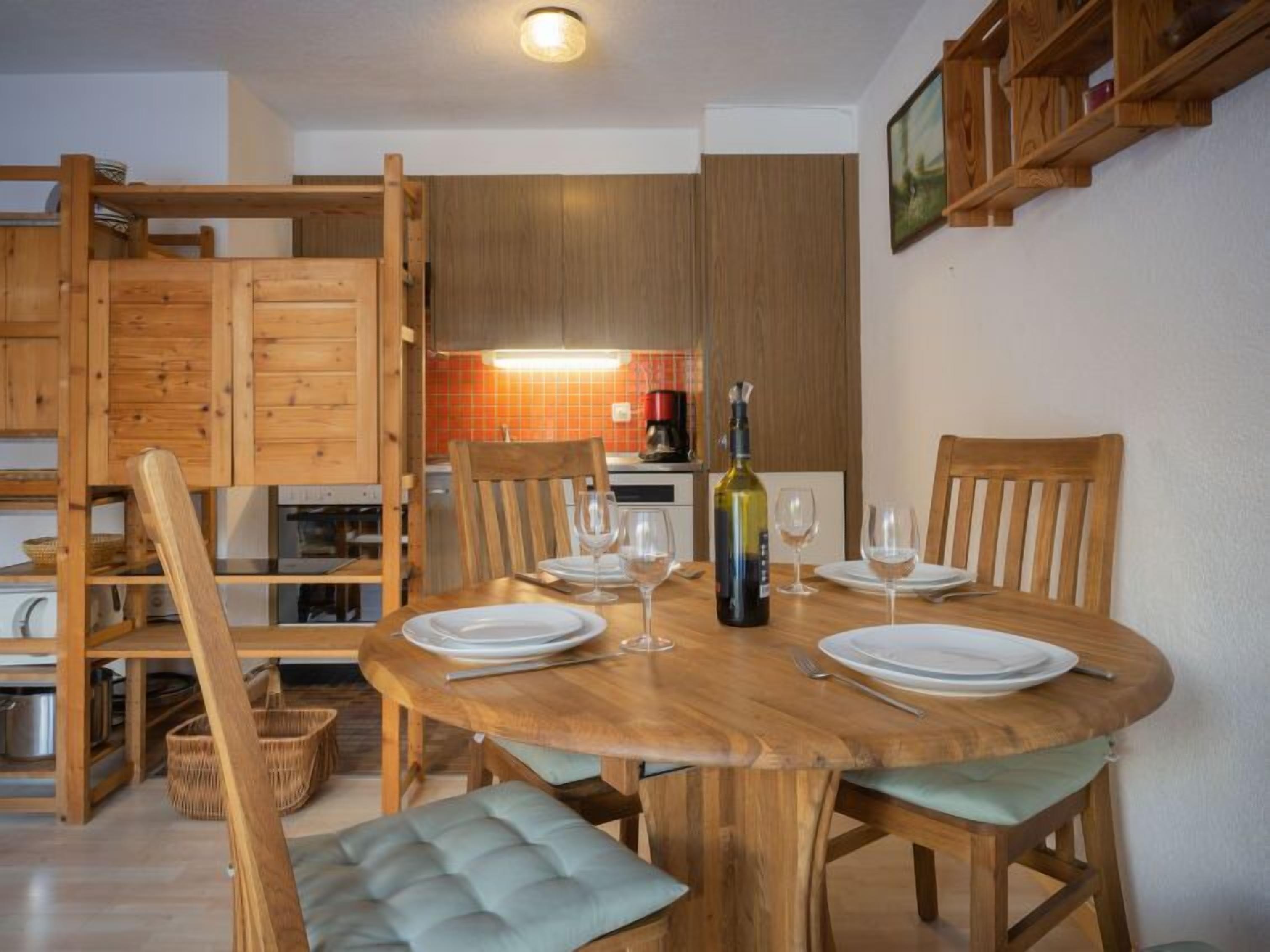Un coin repas avec une table ronde en bois, quatre chaises et une bouteille de vin.