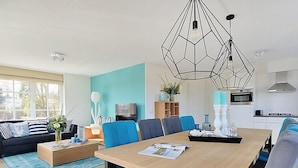 A modern living room with a wooden dining table, blue chairs, a black sofa, and a geometric pendant light. - Tapuit 8 by Interhome (Noordwijk)
