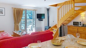 A cozy living room with a red sofa, a dining table set for a meal, a wooden staircase, and a TV mounted on the wall.