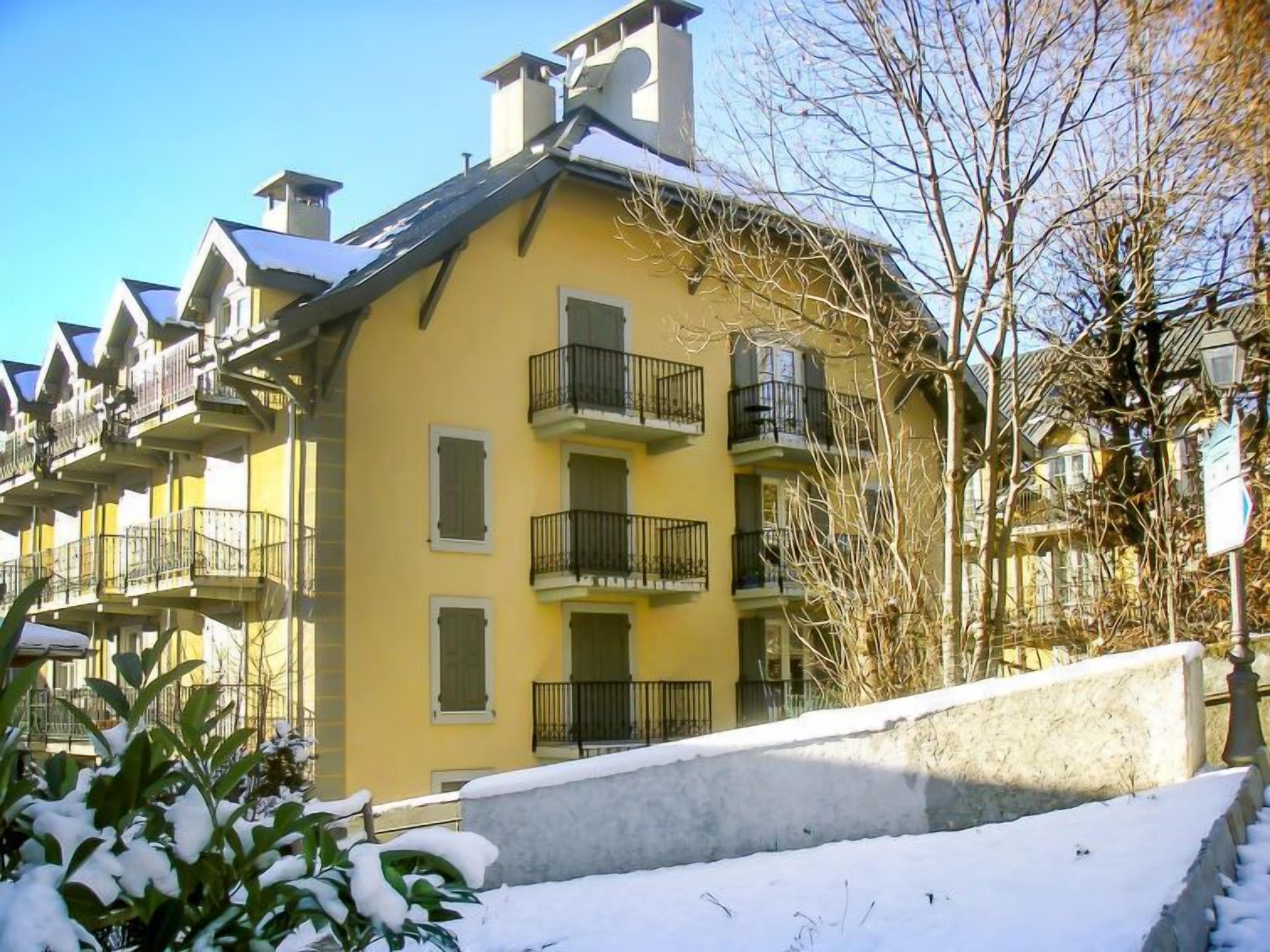Ein gelbes, mehrstöckiges Gebäude mit Balkonen, eine Steinmauer im Vordergrund und Schnee auf dem Boden.