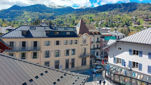 A hotel with a clock tower, a view of mountains, and a town in the background.