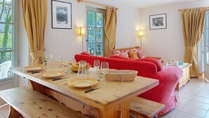 A cozy room with a wooden dining table set for four, a red sofa, and a window with curtains.
