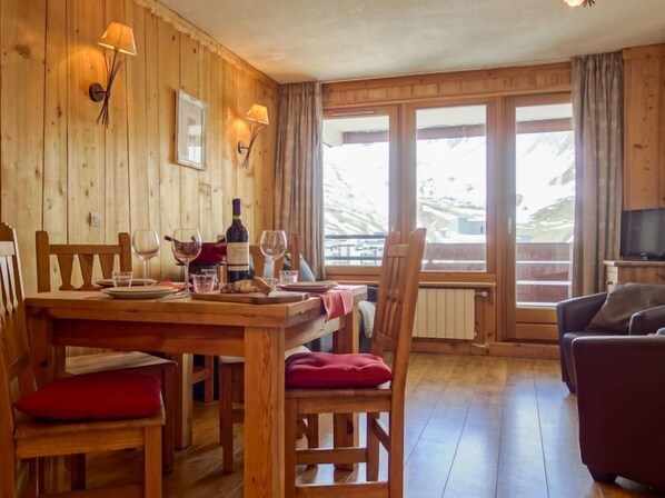 A wooden interior with a dining table set for two, a television, and a view of the outdoors.
