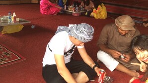 A group of people sitting on the floor in a room with a red carpet, some holding cans and a bottle. - Bedouin expedition Camp (Wadi Rum)