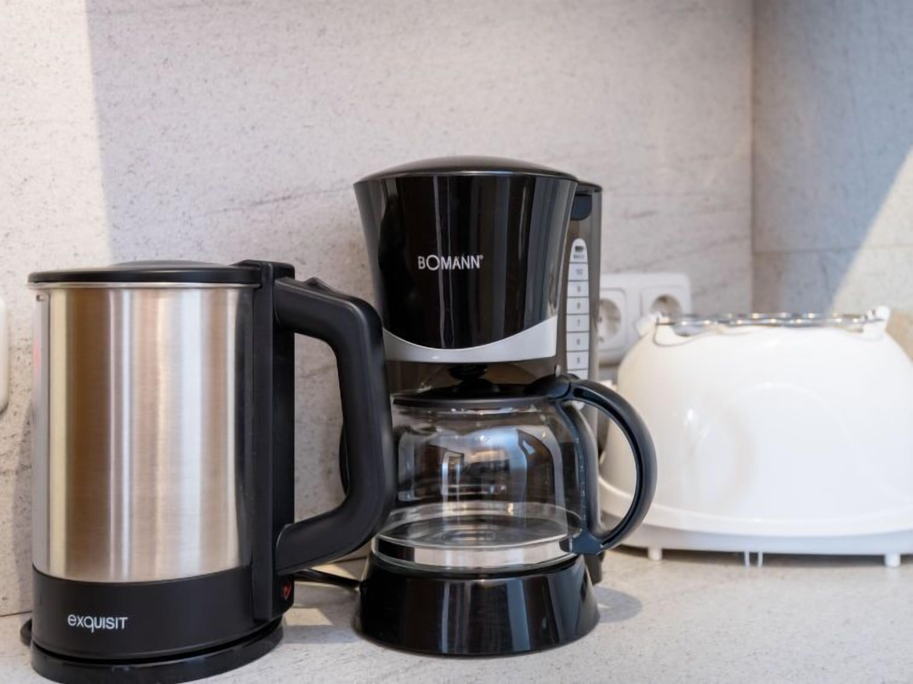 A kitchen with a coffee maker, a stainless steel mug, and a toaster.