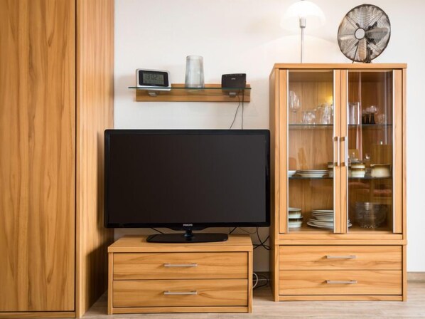 Un salon moderne doté d’un téléviseur à écran plat, de meubles en bois et d’une étagère en verre.