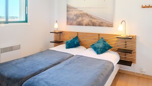 Een slaapkamer met een bed, twee nachtkastjes, een wandlamp en een schilderij van vogels.