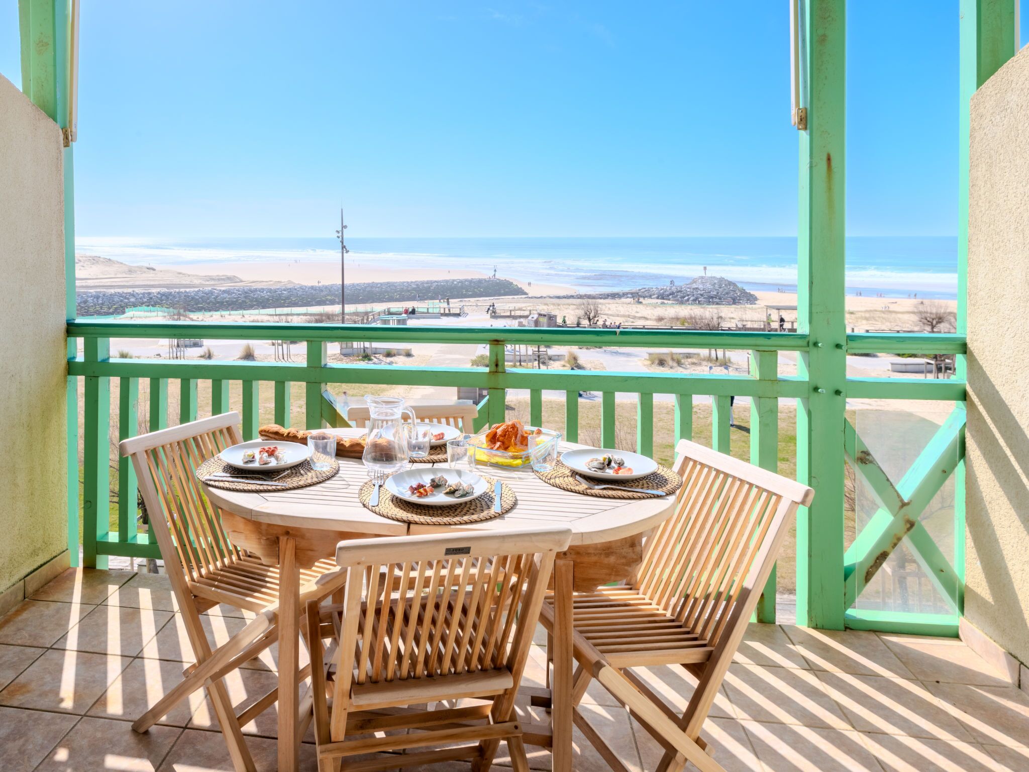 Un balcon avec une table dressée pour un repas, donnant sur une plage.