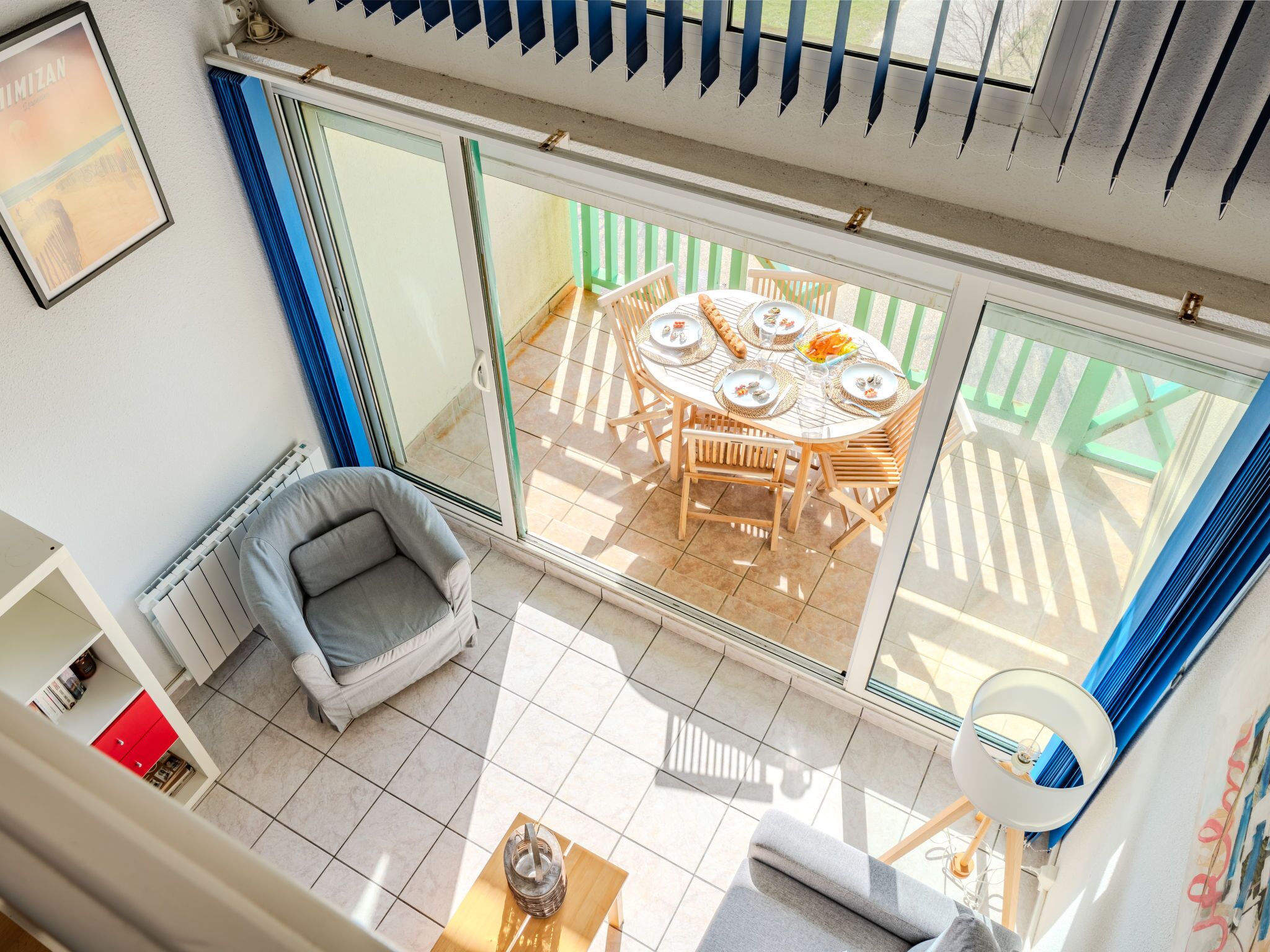 A sunlit patio with a round table and chairs, a cushioned chair, and a small table with a drink.