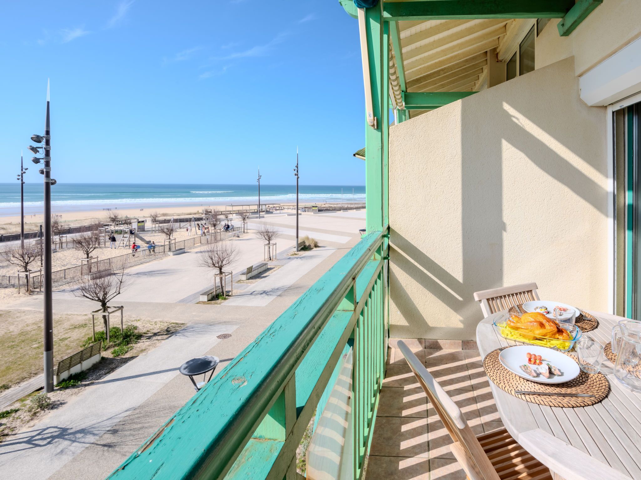 Een balkon met uitzicht op het strand, een tafel met eten en een stoel.