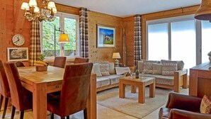 A cozy wooden interior with a dining area, sofa set, and a chandelier. - Sulegg Apt. I by Interhome (Wengen)