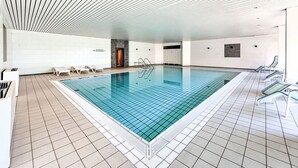 An indoor swimming pool with tiled flooring, a sloped ceiling, and lounge chairs along the sides. - Burgblick (A1110) by Interhome (Lahnstein (Koblenz))