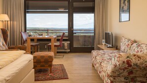 A hotel room with a bed, a sofa, a dining table with chairs, a TV, and a view of the outdoors. - Burgblick (A1110) by Interhome (Lahnstein (Koblenz))