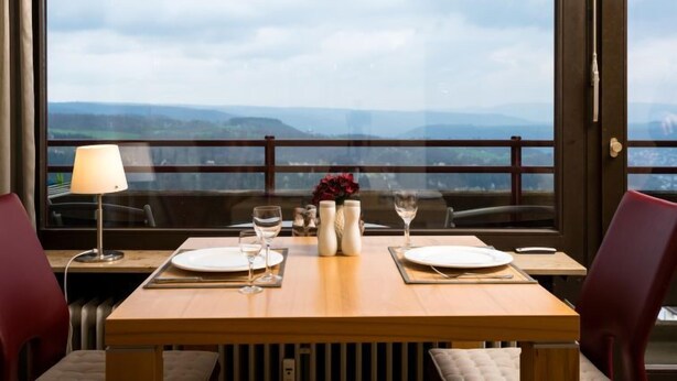 A dining table set with plates, glasses, and a vase with flowers, overlooking a scenic view. - Burgblick (A1110) by Interhome (Lahnstein (Koblenz))