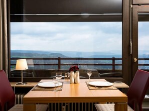 Une table à manger dressée avec des assiettes, des verres et un vase rempli de fleurs, offrant une vue panoramique.